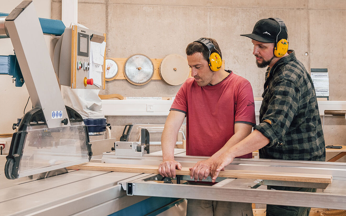 Zwei Männer mit Gehörschutz arbeiten gemeinsam an einer großen Holzbearbeitungsmaschine.