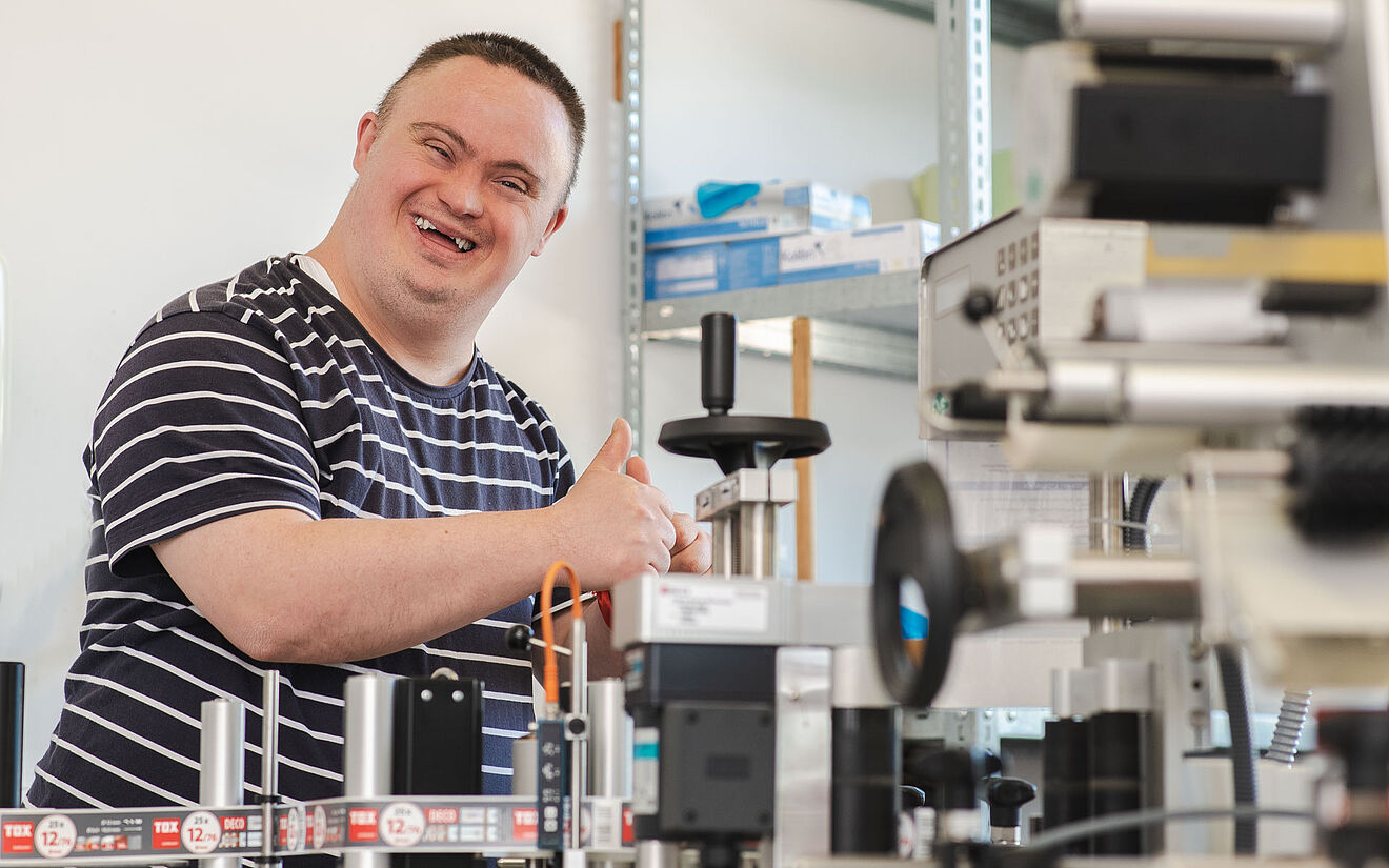 Mann mit Down-Syndrom arbeitet fröhlich an einer Maschine in einer Werkstatt.