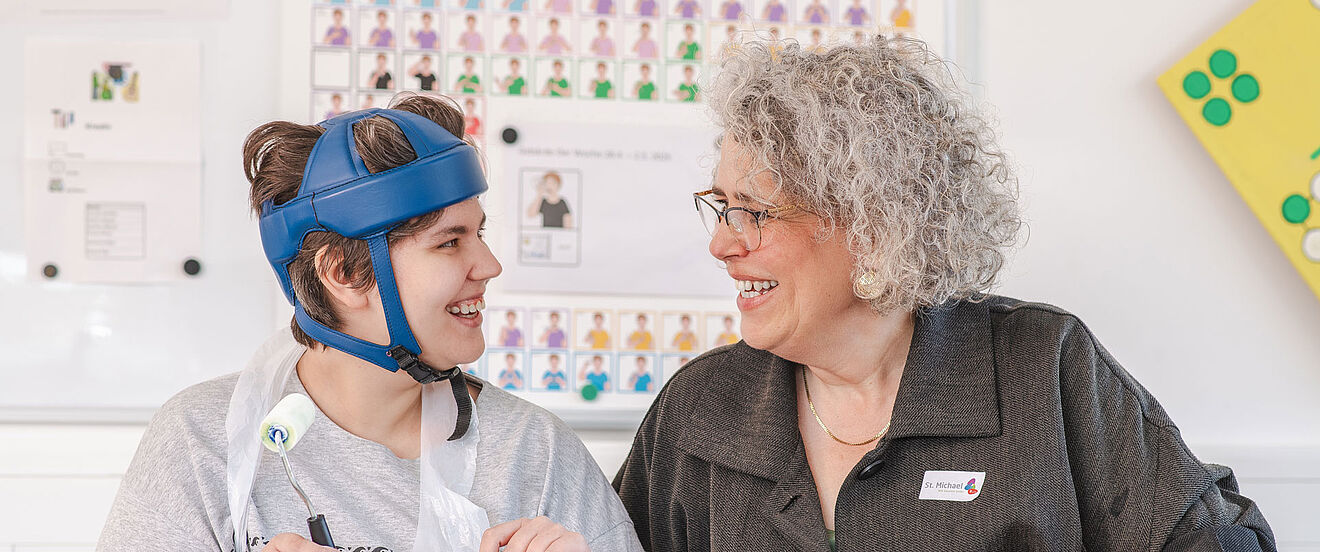 Eine Frau und eine junge Person mit Helm sitzen gemeinsam am Tisch und lachen sich an.